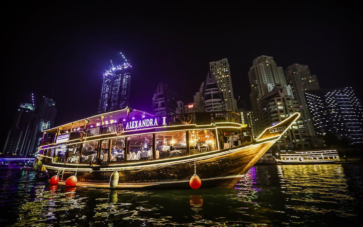 Illuminated dhow cruise boat passing under bridge in Dubai Marina at night