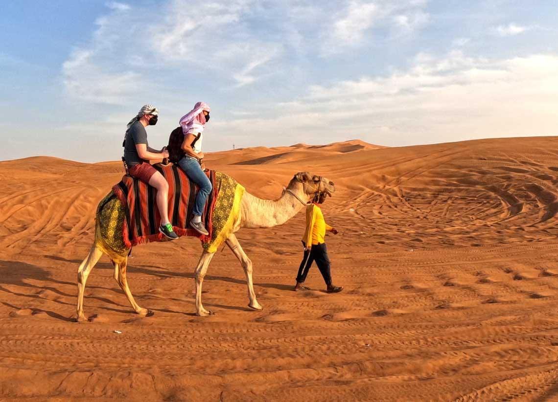 Tourist riding camel at sunset during desert adventure Dubai