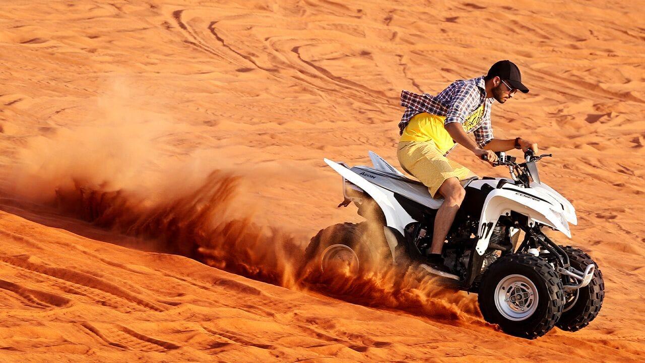 Tourist on ATV quad bike at sunrise during morning desert safari Dubai